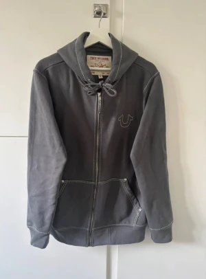Grå hoodie True Religion hoodie!!! - True religion hoodie i storlek M, köpt helt ny och har använts bara några fåtal gånger och har inga defekter. Säljer den för att den är för stor för mig, originella priset 1600. Priset går att diskutera!!😱❤️❤️❤️