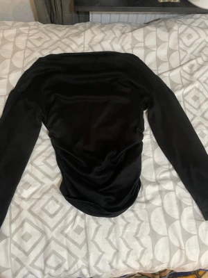 Svart topp med snörning - Snygg svart topp med långa ärmar och cool snörningsdetalj på sidan. Toppen har en tight passform och känns riktigt mjuk och lyxig tack vare sammetstyget. Perfekt för dig som vill sticka ut med en stilren look.