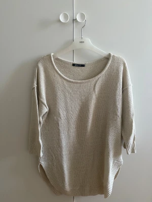 Beige stickad tröja från Gina Tricot - Mysig beige stickad tröja från Gina Tricot med rund halsringning och ribbade muddar vid nederkant och ärmslut. Tröjan har trekvarts ärmar och har en loose passform och är perfekt för lager-på-lager under kyliga dagar. Enkel och stilren design som funkar till många olika looks
