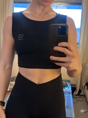 Svart croppad linnetopp Better Bodies - Svart croppad linnetopp från Better Bodies med ribbad struktur och snörning i ryggen. Toppen är ärmlös och har en stilren logga broderad framtill. 