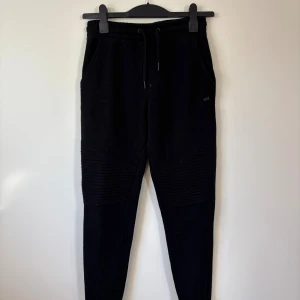 WA mjukisbyxor - 158-164 - Svarta mjukisbyxor från WA med ribbade detaljer över knäna och snörning i midjan. Byxorna har en slim passform och är tillverkade i mjukt bomullsmaterial. 
