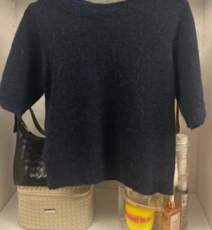 Mörkblå stickad tröja med kort ärm - Mysig mörkblå stickad tröja med korta ärmar och rund hals. Perfekt för lager-på-lager och chill dagar. Materialet är fluffigt och ger en skön känsla, passar dig som gillar enkel och stilren look.