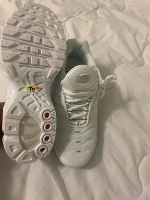 Nike Tn helvita sneakers - Nike Air Max Plus Tn sneakers i helvit färg med mesh och syntetmaterial. Snygga detaljer som Tn Air-logga på häl och innersula, samt synlig Air Max-dämpning i sulan. Rund tå, snörning och platt sula för skön komfort. Perfekt för dig som gillar cleana och sportiga sneakers.