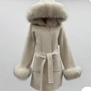 Beige kappa med päls och bälte - Säljer en beige kappa med stor huva och breda muddar i fluffig fuskpäls. Jackan har bälte i midjan för snygg passform och två fickor framtill. Perfekt för dig som vill ha en elegant och mysig look.