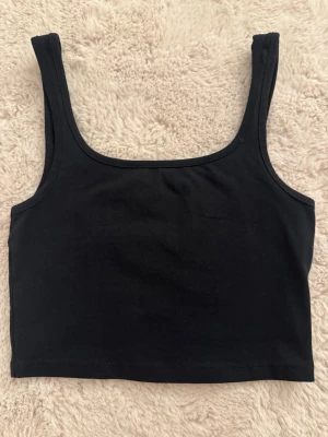 Svart croppad linnetopp - Enkel och stilren svart croppad linnetopp från Xside. Toppen har breda axelband och rak halsringning. Tillverkad i mjuk bomull för en bekväm känsla hela dagen. Nyskick - då den aldrig är använd 
