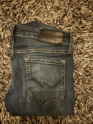 Jack & Jones skinny jeans blå 30/30 - Snygga blå jeans från Jack & Jones med klassisk femficksdesign och diskret slitning. Modellen är skinny med smal passform och normal midja. Materialet är mjukt jeans-tyg som sitter skönt och följer kroppen. Perfekt för dig som gillar en modern look.