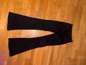 Svarta bootcut LEE jeans - Säljer ett par svarta lee jeans med bootcut-modell och hög midja. Byxorna har klassisk femficksdesign och är tillverkade i ett stretchigt jeanstyg som sitter snyggt över höfterna och låren innan de blir vidare nertill.