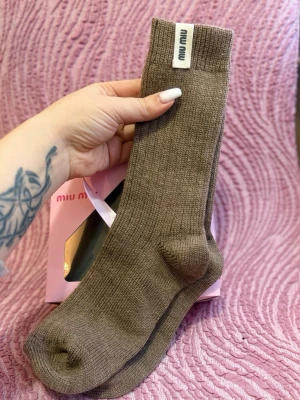 Bruna ribbade strumpor från Miu Miu - Snygga bruna ribbade strumpor från Miu Miu med diskret logotyp på skaftet. Perfekta för dig som vill ha en stilren och trendig look. Strumporna är mjuka och bekväma, tillverkade i bomullsmix som andas.