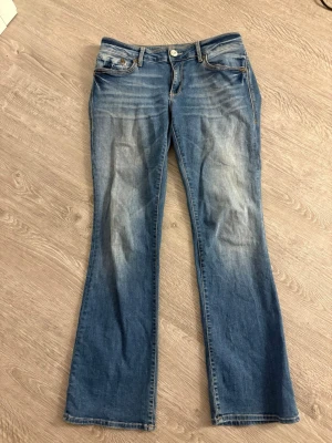 Blå bootcut jeans Bella - Snygga blå jeans från Bella med låg midja och slim bootcut-modell. Jeansen har klassisk femficksdesign, slitningar framtill och kontrastsömmar. Perfekta för dig som gillar en avslappnad men trendig look.