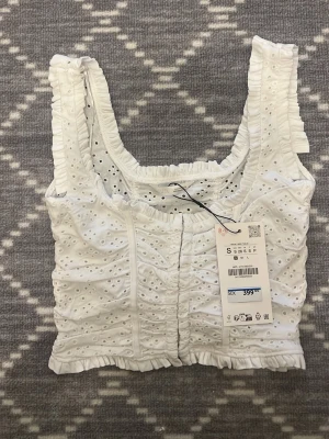 Vit broderad linnetopp från Zara - Superfin vit linnetopp från Zara med broderade detaljer och volangkant. Toppen har breda axelband, fyrkantig ringning och är tillverkad i bomull. Perfekt för en fräsch och somrig look!