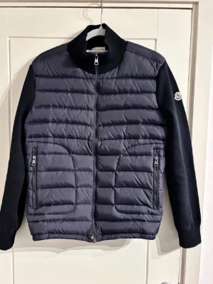  Moncler - Stilren svart overshirt från Moncler med quiltad front och rygg i glansigt material samt ärmar i mjuk bomullsmix. Jackan har två dragkedjefickor fram, ribbad krage och muddar samt Moncler-logga på ärmen. Perfekt för lager-på-lager och streetwear.