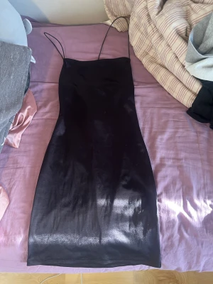 Svart kort  satin klänning med tunna band - Säljer en svart kort klänning i satin med smala axelband och figurnära passform. Klänningen har en enkel, elegant design och slutar ovanför knäna. Perfekt för dig som gillar minimalistisk stil.