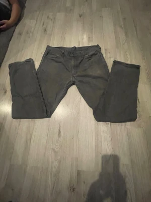 Grå raka jeans med fem fickor - Säljer ett par grå jeans med klassisk femficksmodell och raka ben. Jeansen har bälteshällor och knappgylf. Perfekta till en avslappnad stil och passar till det mesta. Materialet känns som bomull med lite stretch.