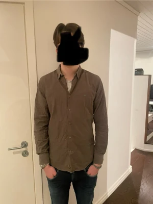 Morris skjorta  - Säljer en Långärmad skjorta från Morris med klassisk krage och knäppning framtill. Skjortan har en liten broderad logotyp på bröstet och är tillverkad i ett mjukt bomullstyg. Perfekt för en stilren och avslappnad look.