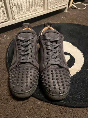 Gråa sneakers med nitar - Snygga grå sneakers med matta nitar på tån och ovandelen. Skorna har en låg profil, rundad tå och är gjorda i mockaliknande material. De har matchande grå skosnören och svart sula. Perfekta för dig som vill sticka ut med en edgy stil. (Några spikar saknas) 