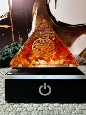 Orogonit pyramid karneol livets blomma  - Denna orgonitpyramid kombinerar karneolens livskraft med Livets blommas heliga geometri för att skapa ett kraftfullt energiverktyg som stärker kreativitet, motivation och jordad handlingskraft.  🧡 Karneol aktiverar sakralchakrat och sägs öka glädje, mod, passion och kreativt flöde. 🌸 Livets blomma symboliserar universell harmoni, balans och skapandets grundmönster. 🌀 Orgonitens uppbyggnad (kristaller, metall och kopparspiral) sägs rena och omvandla stillastående eller tung energi till positiv