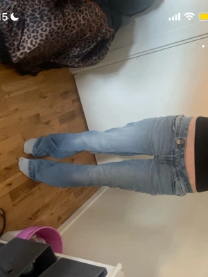 Ljusblå bootcut jeans - Säljer ett par ljusblå bootcut jeans med låg midja och klassisk femficksdesign. Jeansen har en snygg tvättad look och är perfekta för dig som gillar en avslappnad men trendig stil. Materialet är denim i bomull.