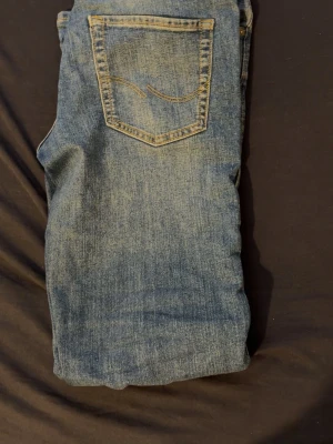 Blå jeans med klassisk passform - Säljer ett par blå jeans i klassisk modell med fem fickor och snygga kontrastsömmar. Jeansen har en normal midja och raka ben. Materialet är slitstark denim i bomull. Perfekt för dig som gillar en tidlös och enkel stil.