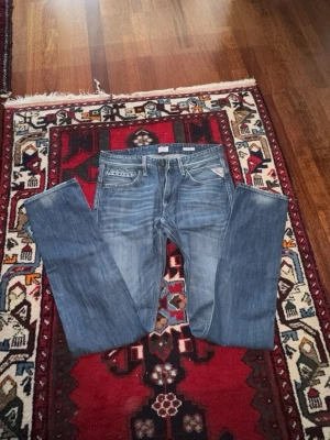 Blå raka jeans med slitningar - Säljer ett par klassiska blå jeans med raka ben och snygga slitningar. Jeansen har fem fickor och normalhög midja. Perfekta för en avslappnad och trendig look. Materialet är denim i bomull.