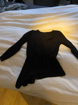 Svart omlottopp med lång ärm - Snygg svart omlottopp med långa ärmar och lätt utsvängd nederdel. Toppen har en omlottdesign framtill som ger en stilren look. 