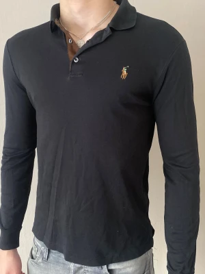 Svart långärmad piké från Ralph Lauren - Klassisk svart långärmad pikétröja från Ralph Lauren med den ikoniska broderade loggan på bröstet. Tröjan har krage, knappar vid halsen och är tillverkad i mjuk bomull. Perfekt till allt. Postar inom 24h📦 köp budle på mer än ett plagg för 10% rabbat🤝