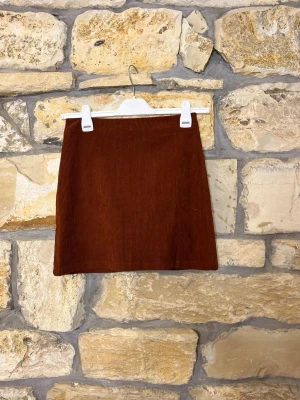 Brun/roströd manchesterkjol i kort modell - Snygg brun/roströd kortkjol i manchester med enkel, rak passform. Kjolen har en klassisk look och passar perfekt till både stickade tröjor och t-shirts. Perfekt för dig som gillar retrovibbar och vill ha en tidlös bas i garderoben.