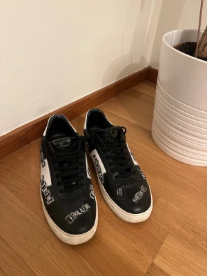 Valentino Flycrew - Jamie Reid Collab - Unika svartvita sneakers från Valentino med textapplikationer och coola nitar runt sulan. Exklusiva skor med Jamie Reid collab samt som var en gång släpp och inte produceras längre. Såklar Äkta! Ops: Bara en spik som saknas.