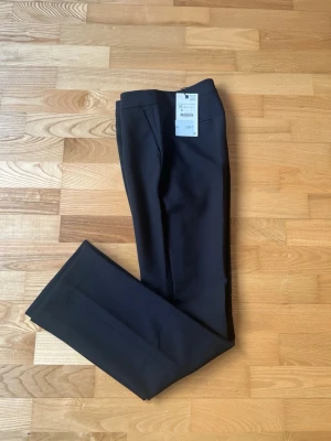 Svarta kostymbyxor från Zara - Klassiska svarta kostymbyxor från Zara med rak passform och pressveck. Byxorna har diskreta sidofickor och är tillverkade i ett mjukt material som ger en stilren look. Perfekta för en clean och modern outfit.