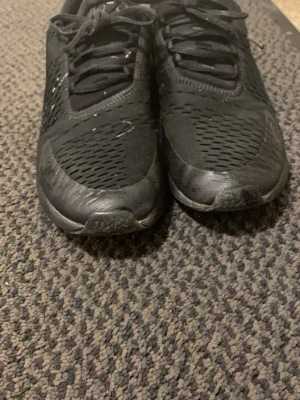 Svarta Nike Air Max sneakers - Säljer ett par helsvarta Nike Air Max sneakers med klassisk låg profil. Skorna har ventilerande mesh-ovandel och detaljer i syntetmaterial. Swoosh-logga på sidan och snörning framtill. Perfekta för dig som gillar sportig och stilren look.