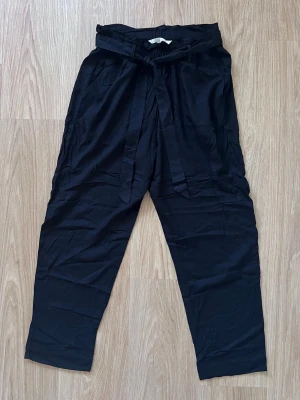 Svarta kostymbyxor med knytskärp från H&M, storlek 40 - Svarta linnebyxor från H&M med hög midja och knytband i midjan. Byxorna har raka ben och sidfickor. Fuskfickor bak. Mycket bra kvalitet! 100% viskos.