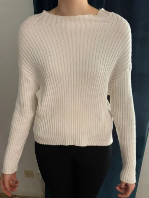 Vit ribbstickad tröja  - Säljer en stilren vit ribbstickad tröja med boatneck och långa ärmar. Tröjan har en avslappnad passform och är tillverkad i ett mjukt, stretchigt material som känns skönt mot huden. Använd ett fåtal gånger och är i mycket bra skick. 