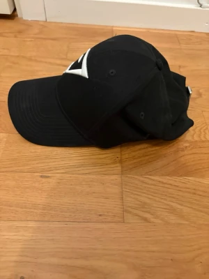 Svart keps från Gymshark - Snygg svart keps från Gymshark med böjd skärm och justerbar rem baktill. Kepsen har en vit broderad Gymshark-logga framtill och är tillverkad i ett slitstarkt tygmaterial. Perfekt accessoar för en sportig och stilren look.