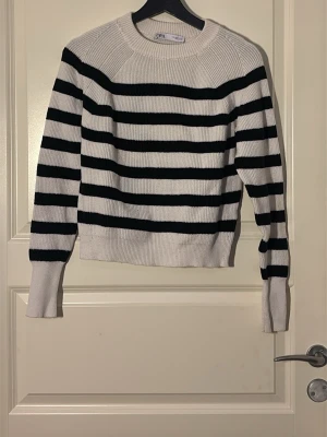 Randig stickad tröja från Zara - Snygg stickad tröja från Zara med breda svarta och vita horisontella ränder. Tröjan har rund halsringning, långa ärmar och ribbade muddar vid ärmslut och nederkant. Perfekt för dig som gillar klassisk och enkel stil.