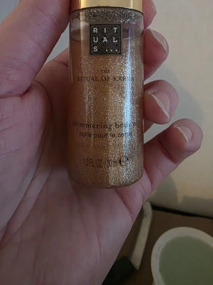 Rituals Shimmering Body Oil guld - Shimmering body oil från Rituals i serien The Ritual of Karma. Oljan har en skimrande guldig färg och kommer i en genomskinlig flaska med guldfärgat lock. Perfekt för att ge huden en glittrande finish.