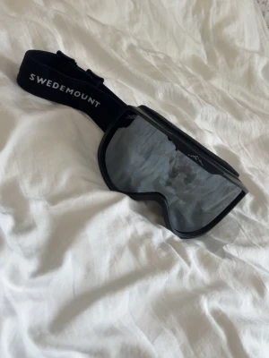 Svarta skidglasögon Swedemount - Säljer ett par svarta skidglasögon från Swedemount med spegeltonade linser och justerbart elastiskt band. Snygg och sportig design, perfekt för dig som gillar vintersport och vill ha ett par stilrena goggles.
