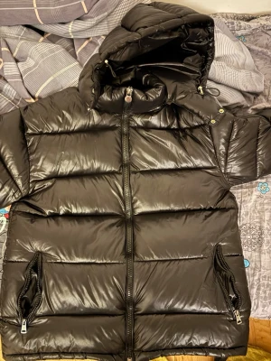 Svart pufferjacka från Moncler - Säljer en svart pufferjacka från Moncler med glansig finish och stor huva. Jackan har dragkedja framtill, två fickor med dragkedja och klassisk Moncler-logga på armen. Perfekt för kalla dagar och riktigt snygg till streetwear-stilen. Storlek S/M, 2000 för jackan men pris kan diskuteras 