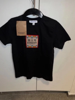 Svart Burberry t-shirt med rutig patch - Snygg svart t-shirt från Burberry med klassisk rutig patch och logga på bröstet. T-shirten har rund hals och korta ärmar. Tillverkad i mjuk bomull för skön känsla och stilren look.