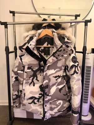 Canada goose whyndham, Camouflage  - Säljer en riktigt fet dunjacka från Canada Goose i grått, vitt och svart camomönster. Jackan har stor huva med fluffig prärjevar pälskant och tydlig logga på ärmen. Perfekt för kalla vinterdagar och riktigt snygg streetstil. 1:1 äkta päls