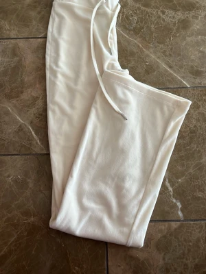 Vita mjukisbyxor med dragsko - Säljer ett par vita mjukisbyxor med raka ben och dragsko i midjan. Byxorna är gjorda i ett mjukt och skönt material, perfekta för chill dagar hemma eller när du vill vara bekväm. Inga synliga loggor eller märken.