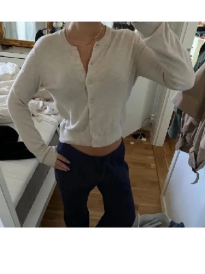 Beige cropped kofta med knappar - Snygg beige kofta med rund hals och knäppning framtill. Modellen är croppad och har långa ärmar samt ribbade muddar. Perfekt att styla med jeans eller kjol för en chill look.