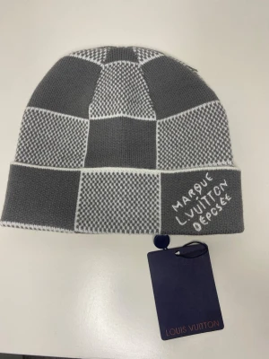 Beanie Louis Vuitton 🧢 - This Louis Vuitton beanie features a stylish checkered pattern in grey and white. It appears to be in excellent condition with tags attached.  ⭐️ Condition: 10/10 🎨 Color: Grey and White 📦 Fast and careful shipping