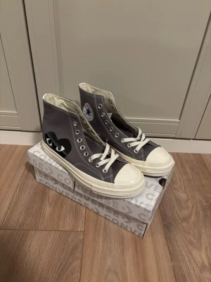 Converse x CDG Play grå high tops - Cdg X converse storlek 41. Helt nya med box. Nypris 1600 mitt pris 1099. Snygga Converse x Comme des Garçons Play high tops i grå canvas med vit tå och sula. Ikoniskt svart hjärta med ögon på sidan och klassisk Converse-logga på insidan. Perfekta för dig som vill sticka ut med en stilren och trendig sneaker.