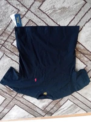 Marinblå t-shirt från Polo Ralph Lauren - Snygg marinblå t-shirt från Polo Ralph Lauren med klassisk passform och korta ärmar. T-shirten har en liten rosa logga broderad på bröstet och är tillverkad i mjuk bomull. Perfekt till jeans eller shorts för en clean look.