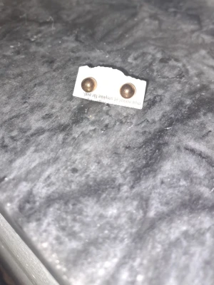 Runda gulliga  pärlörhängen - Snygga örhängen med rund form och brun pärldesign. De är små och diskreta, perfekta för dig som gillar minimalistiska accessoarer. Metallfärgen är varm och ger ett stilrent intryck.