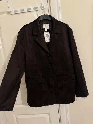 Mörkbrun kavajjacka från H&M - Snygg mörkbrun kavajjacka från H&M i mockaimitation strl XL. Säljes pga hann ej rerurnera i tid