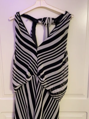 Svartvit randig långklänning - Snygg långklänning med svartvita diagonala ränder och knyt i nacken. Klänningen har ett unikt mönster och är ärmlös med öppen rygg. Tillverkad i ett lätt, luftigt material som ger ett elegant fall.