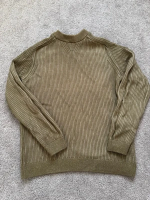 Olivgrön stickad tröja These Glory Days - Snygg olivgrön stickad tröja från These Glory Days. Tröjan har ribbstickat mönster, rund halsringning och långa ärmar. Perfekt för dig som vill ha en lite unik stickad tröja.                                      Bara att höra av sig vid eventuella frågor!