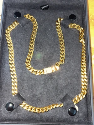 Guldfärgat kedjehalsband Kejsar - Snyggt guldfärgat halsband från Kejsar med klassisk cuban chain-design. Halsbandet har en bred, platt länk och ett robust lås. Kommer i en svart ask med Kejsar-logga i guld. Perfekt accessoar för att lyfta din outfit.