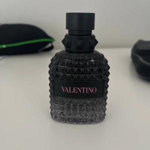 Valentino parfym med nitar - Snygg parfymflaska från Valentino i svart glas med coolt nitat mönster och svart lock. Flaskan har en lyxig och modern design med Valentino-loggan i rosa på svart etikett. Perfekt för dig som gillar exklusiva dofter och stilren inredning.   Ca 75% kvar