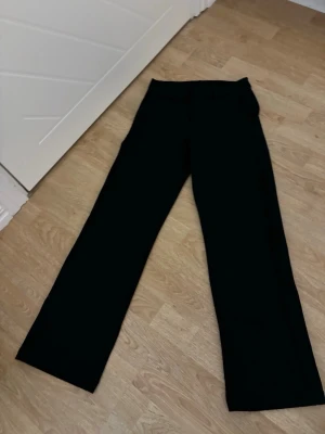 Svarta kostymbyxor med raka ben - Snygga svarta kostymbyxor med klassisk rak passform och midja. Byxorna har en stilren look och är perfekta till en dressad outfit. Materialet känns mjukt och följsamt, och de har hällor för bälte. Passar dig som gillar enkel och clean stil.